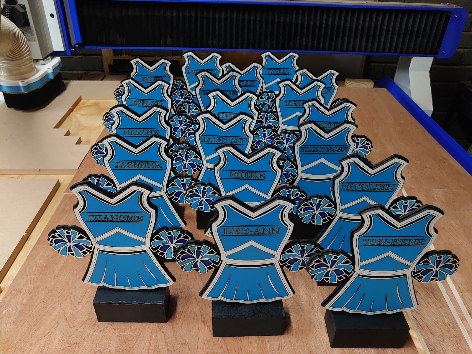 A batch of finished cheerleading trophies on the workbench next to the laser cutter